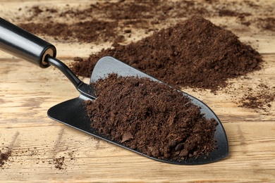 Photo of Metal gardening trowel with soil on wooden table