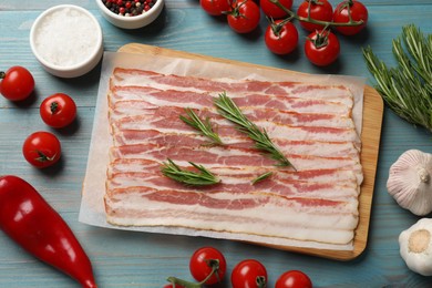 Slices of raw bacon and fresh products on light blue table, flat lay