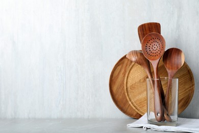 Set of wooden kitchen utensils and plates on light grey table. Space for text