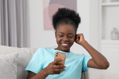 Photo of Happy young woman using smartphone on sofa at home