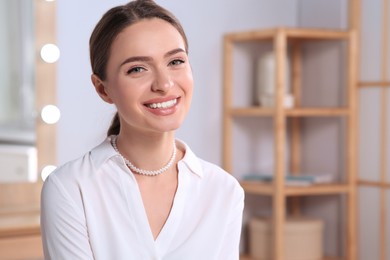 Young woman wearing elegant pearl necklace indoors, space for text
