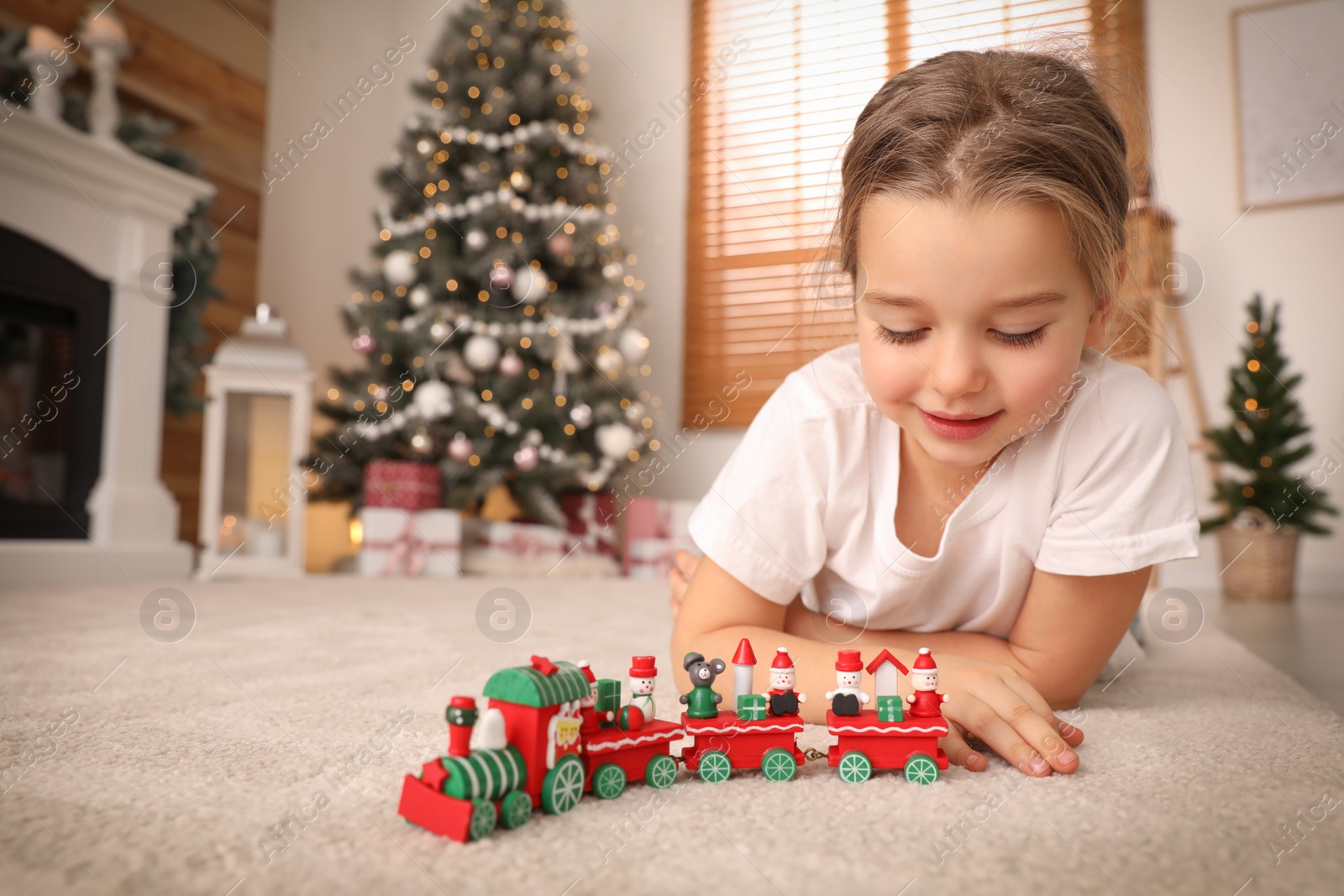 Photo of Little girl playing with colorful train toy in room decorated for Christmas