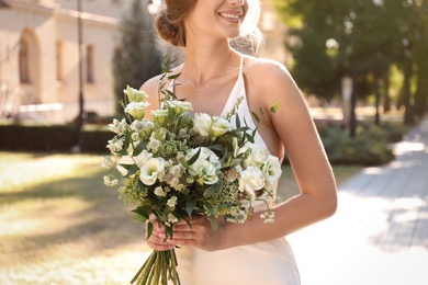Bride in beautiful wedding dress with bouquet outdoors, closeup