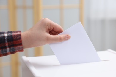 Photo of Woman putting her vote into ballot box on blurred background, closeup