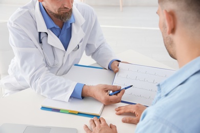 Photo of Male doctor showing cardiogram to patient in clinic. Cardiology consultation