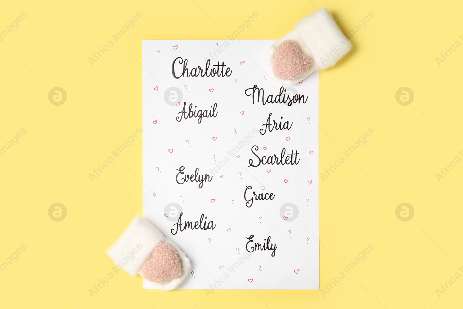 Photo of List of different baby names and newborn mittens on yellow background, flat lay