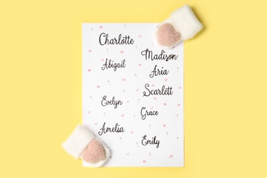 Photo of List of different baby names and newborn mittens on yellow background, flat lay