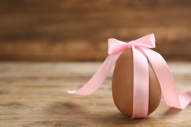 Sweet chocolate egg with pink bow on wooden table. Space for text