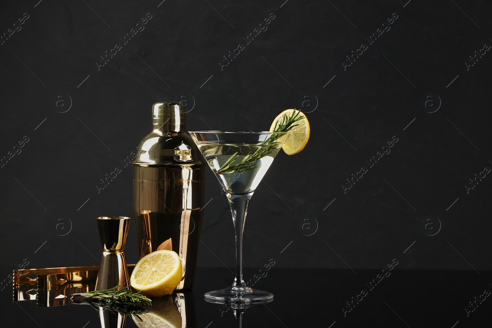 Photo of Martini cocktail with lemon slice, rosemary, shaker and fresh fruit on black background