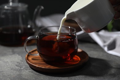 Photo of Pouring milk into cup of tea on grey table, closeup