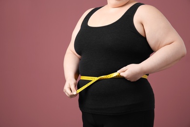 Overweight woman with measuring tape on color background