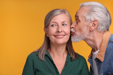 Photo of Senior man kissing his beloved woman on orange background, space for text