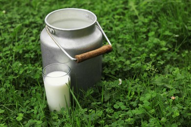 Can and glass with fresh milk on green grass outdoors