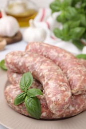 Raw homemade sausages and basil leaves on plate, closeup