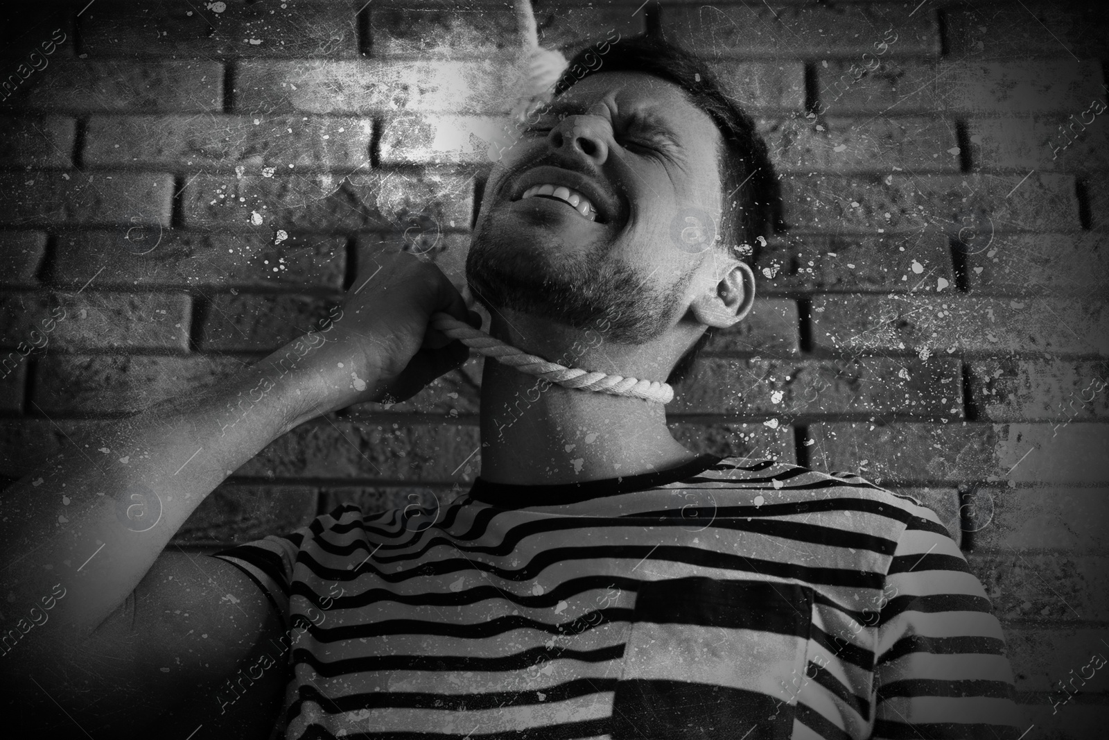 Image of Depressed man with rope noose on neck near brick wall, low angle view. Suicide concept