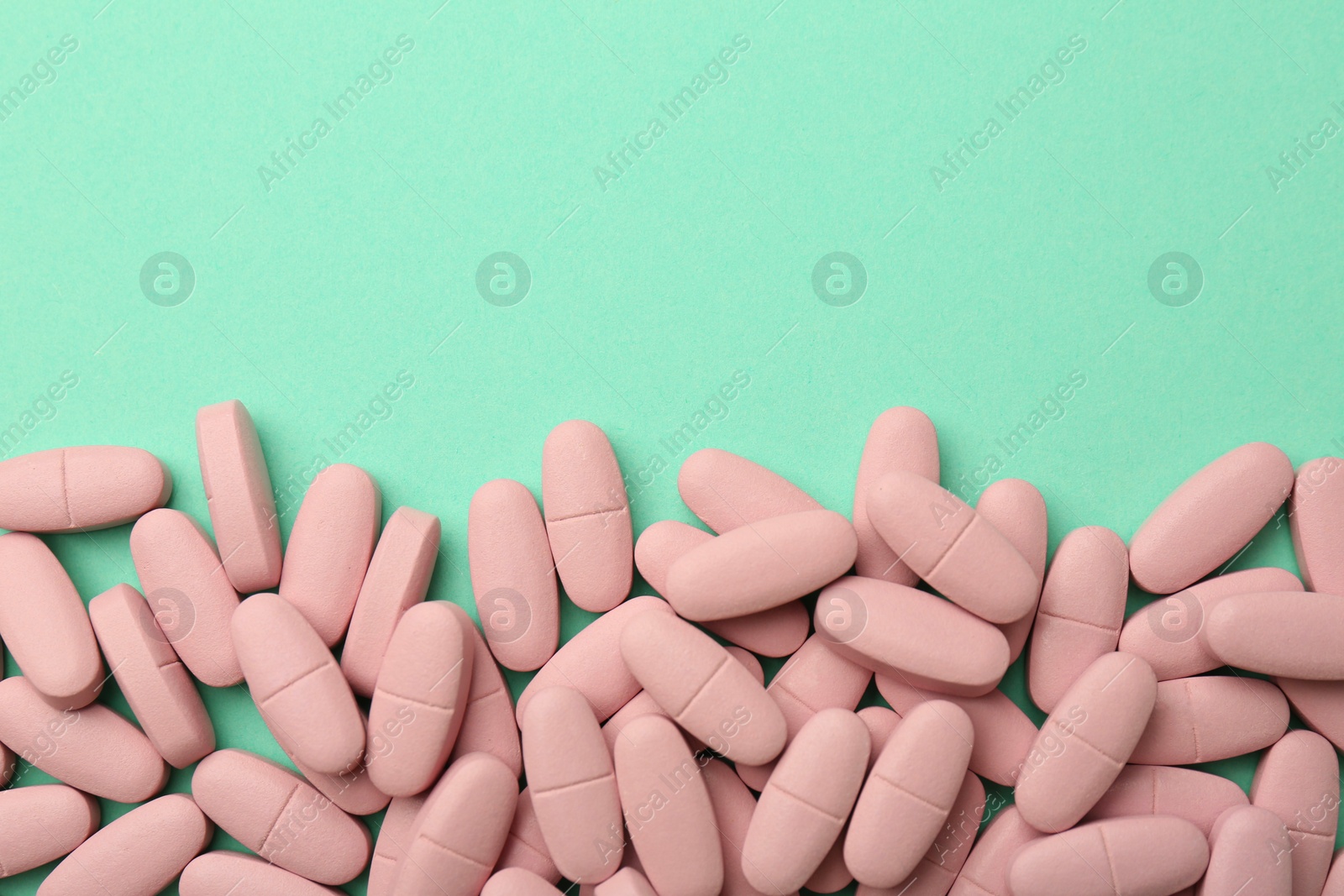 Photo of Pink vitamin capsules on turquoise background, top view. Space for text