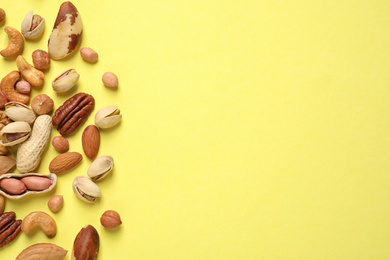 Different delicious nuts on yellow background, flat lay. Space for text