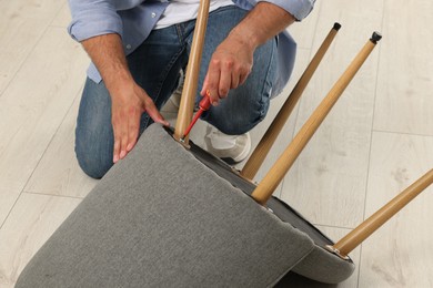 Photo of Man with screwdriver assembling armchair on floor, closeup
