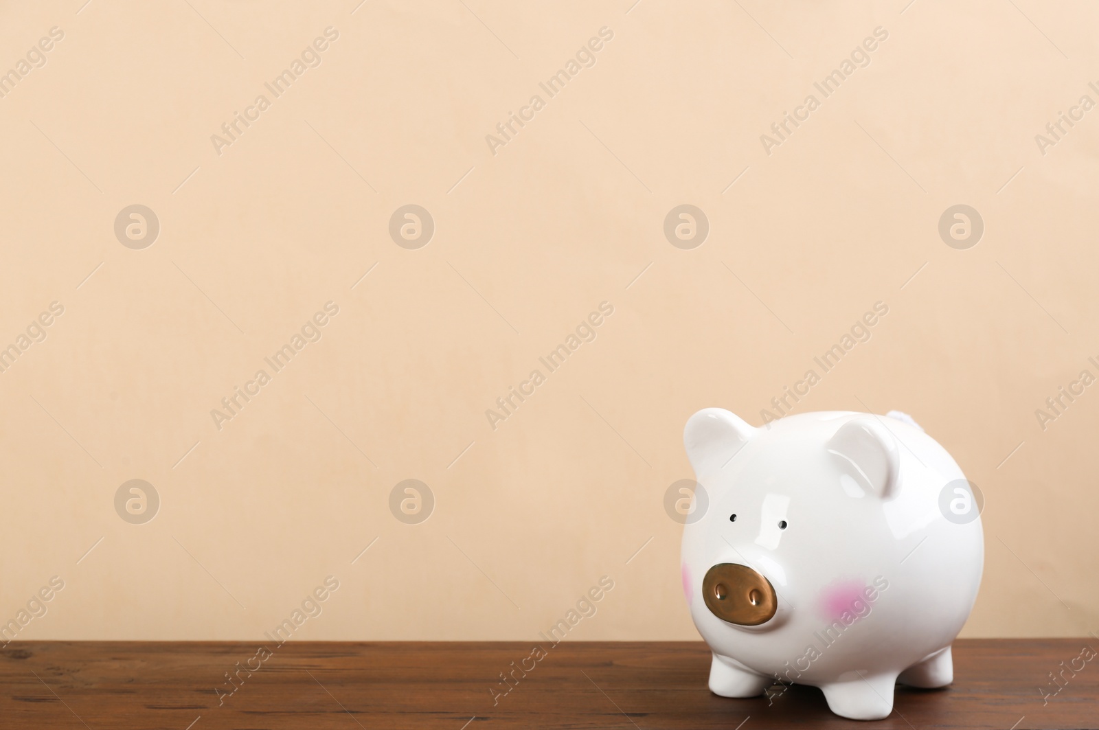 Photo of White piggy bank on wooden table against beige background. Space for text