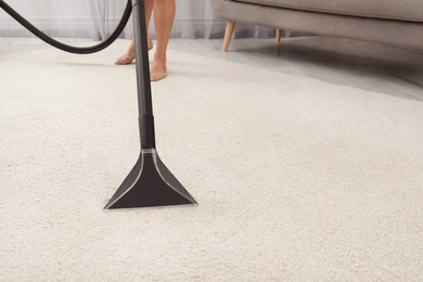 Photo of Woman removing dirt from carpet with vacuum cleaner indoors, closeup. Space for text