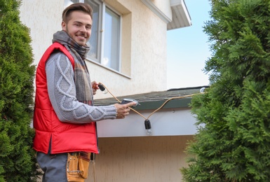 Young man decorating roof with Christmas lights