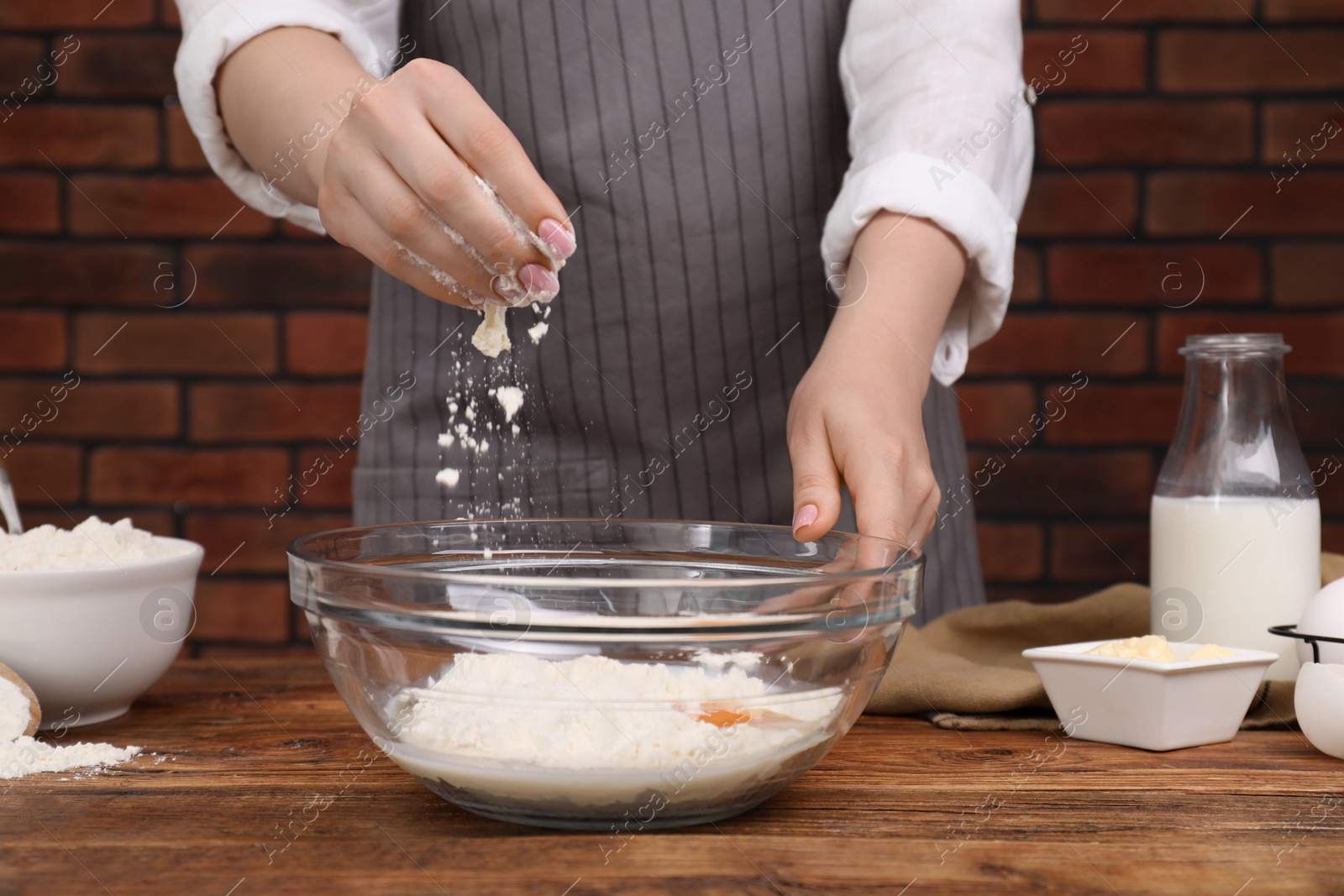Photo of Preparing tasty baklava. Woman adding flour into bowl at wooden table, closeup