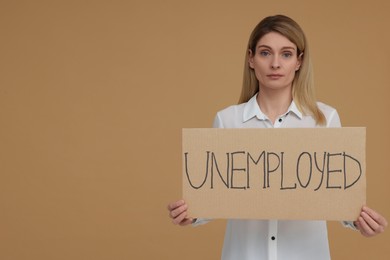 Photo of Woman holding sign with word Unemployed on beige background. Space for text