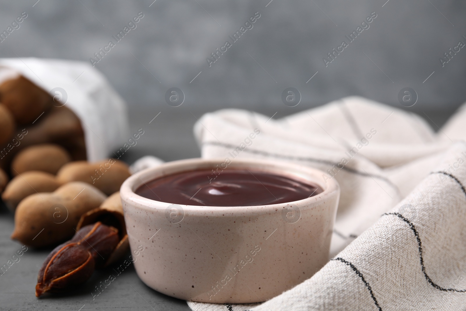 Bowl of tamarind sauce and fresh pods on grey wooden table, space for text Photo of Bowl of tamarind sauce and fresh pods on grey wooden table, space for text