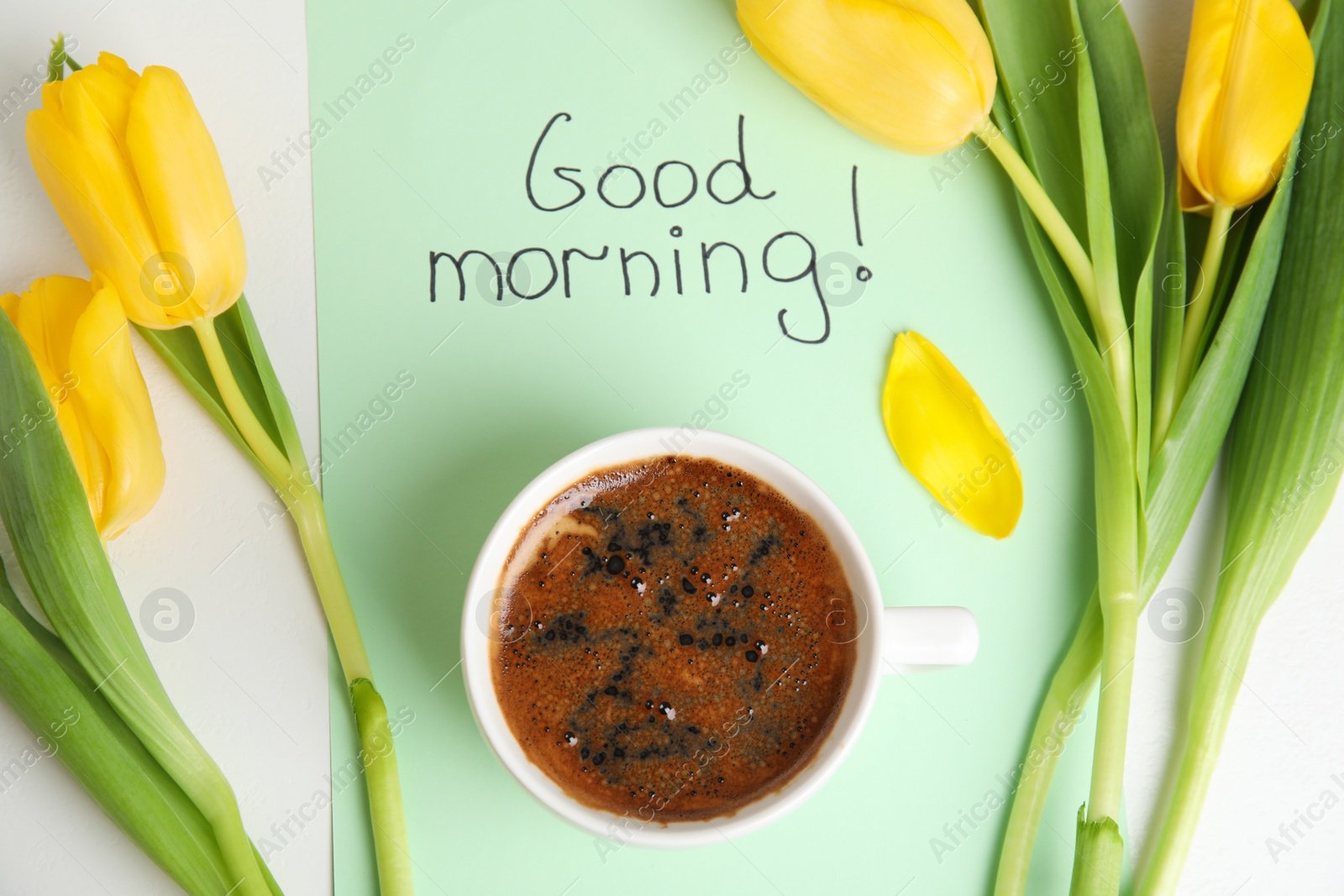Photo of Aromatic coffee, beautiful flowers and card with words GOOD MORNING on white table, flat lay