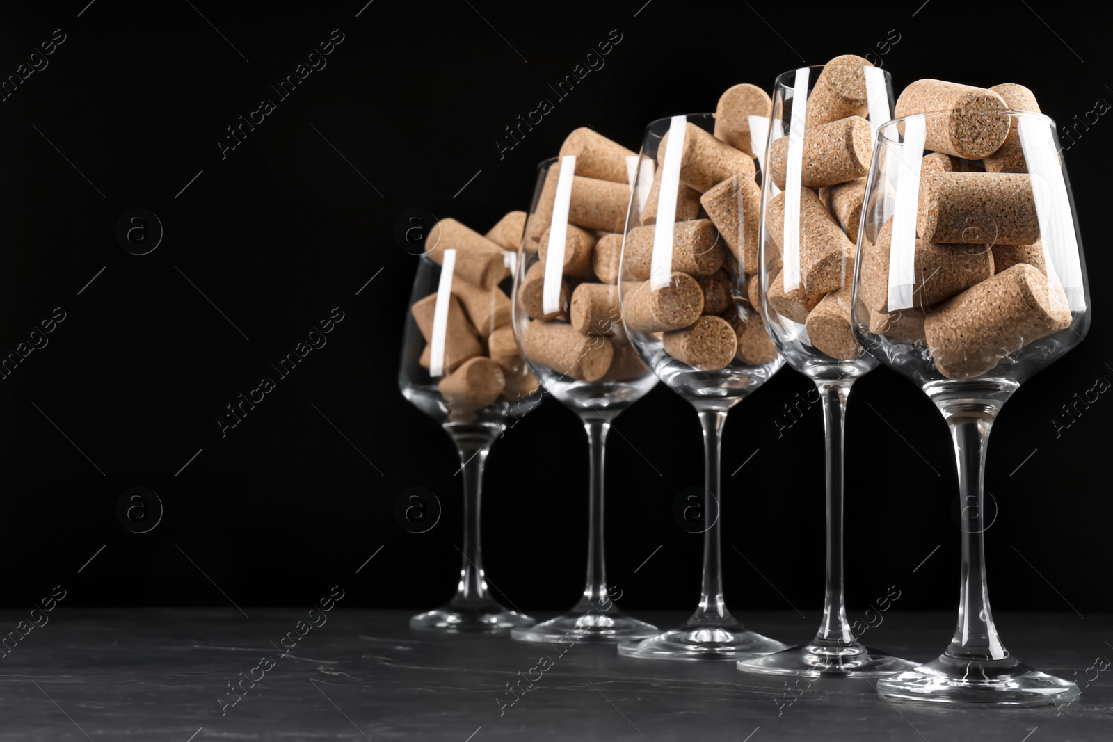 Photo of Glasses full of wine corks on black table. Space for text