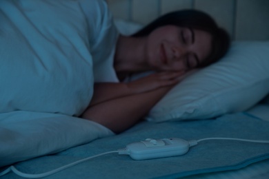 Photo of Young woman sleeping in bed with electric heating pad, focus on cable