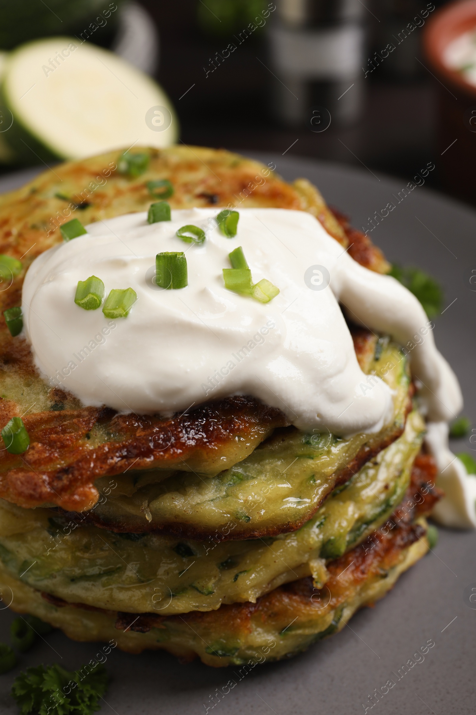 Photo of Delicious zucchini fritters with sour cream on plate, closeup view
