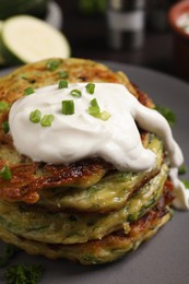 Delicious zucchini fritters with sour cream on plate, closeup view