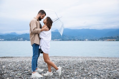 Photo of Young couple with umbrella enjoying time together under rain on beach, space for text