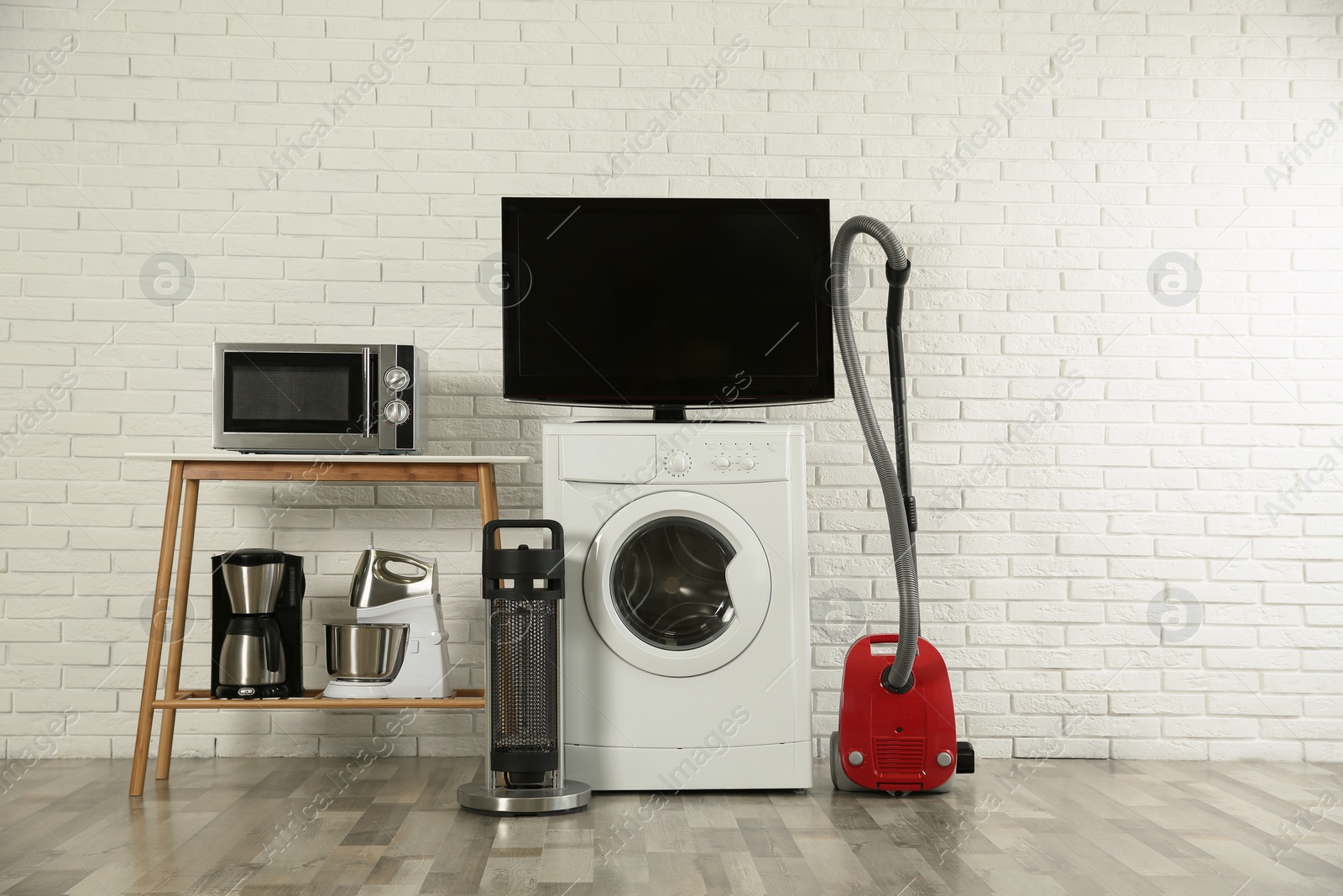 Photo of Modern vacuum cleaner and different household appliances near white brick wall indoors