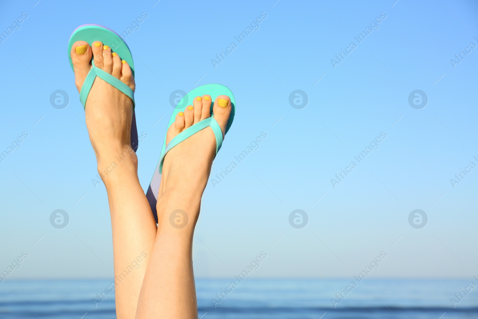 Photo of Closeup of woman wearing flip flops near sea, space for text. Beach accessories