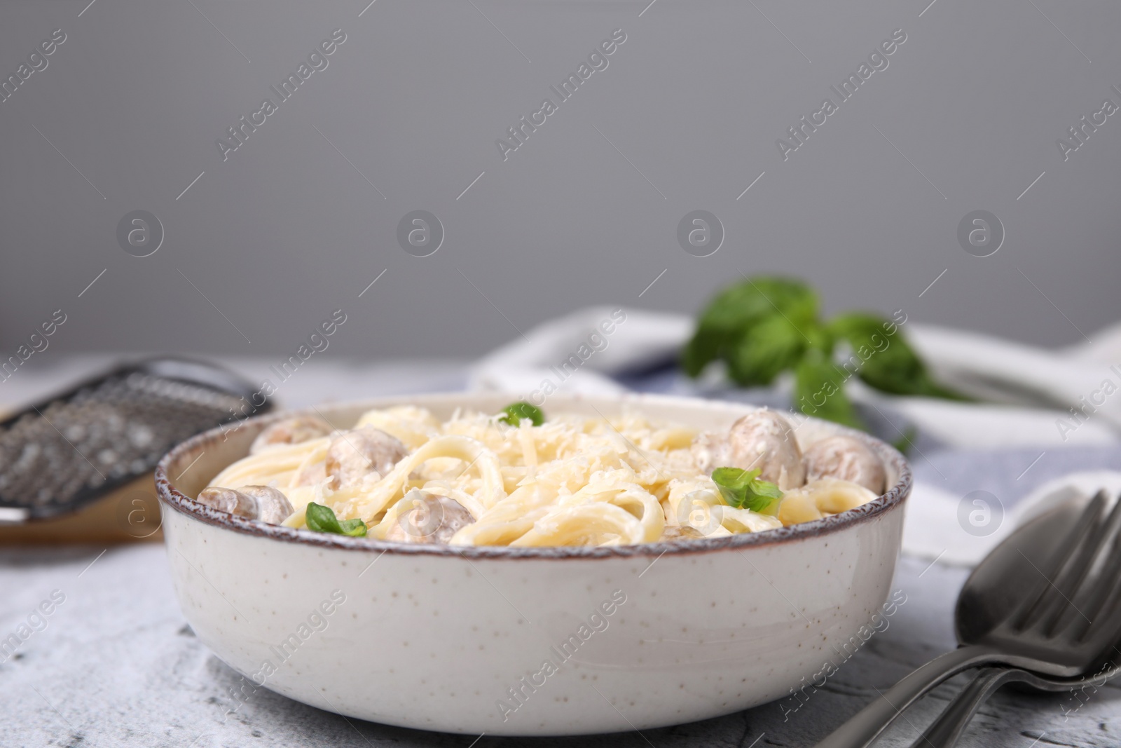 Photo of Delicious pasta with mushrooms and cheese served on light grey textured background, closeup