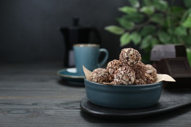 Photo of Bowl of delicious sweet chocolate candies on black wooden table, space for text