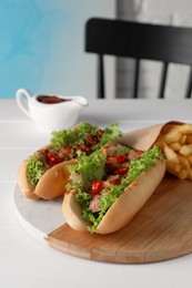 Tasty hot dogs with chili, lettuce, sauce and French fries on white wooden table, closeup