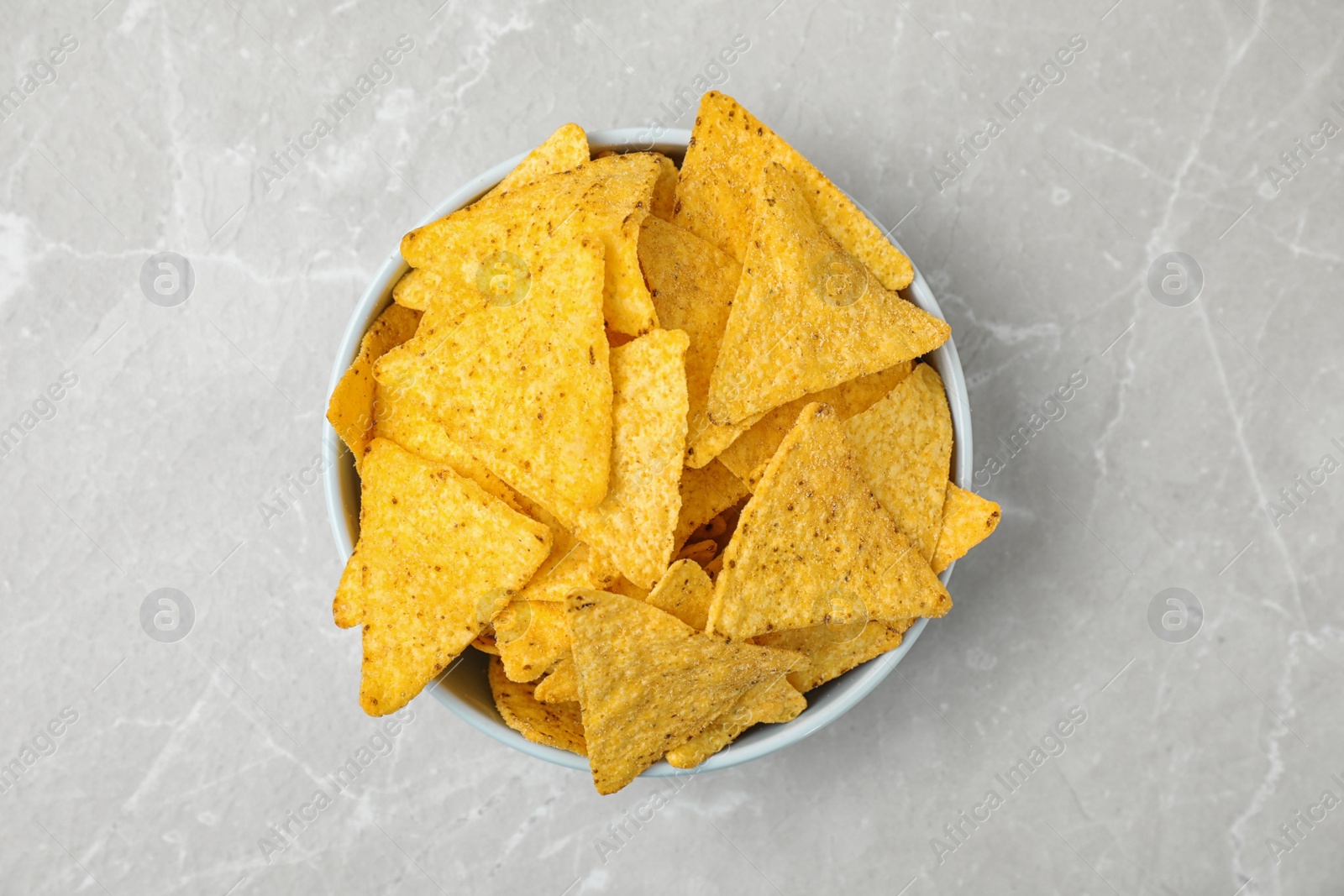 Photo of Bowl with tasty Mexican nachos chips on grey table, top view