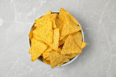 Bowl with tasty Mexican nachos chips on grey table, top view