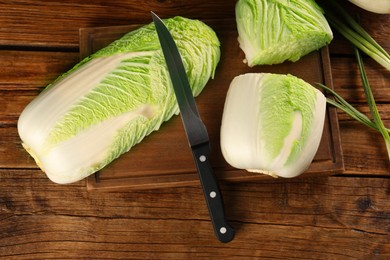 Photo of Fresh Chinese cabbages, green onion and knife on wooden table, flat lay