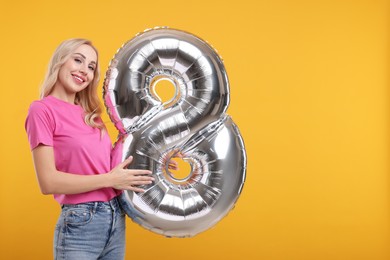 Photo of Happy Women's Day. Charming lady holding balloon in shape of number 8 on orange background