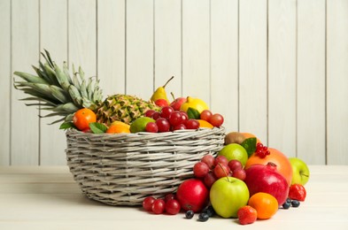 Photo of Wicker basket with different fresh fruits on white wooden table