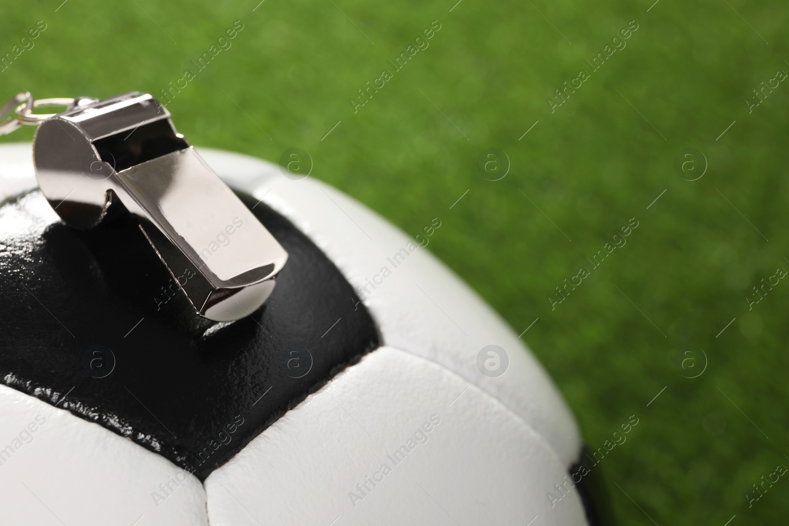 Photo of Football referee equipment. Soccer ball and metal whistle on green grass, closeup with space for text