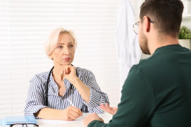 Photo of Doctor consulting patient at white table in clinic