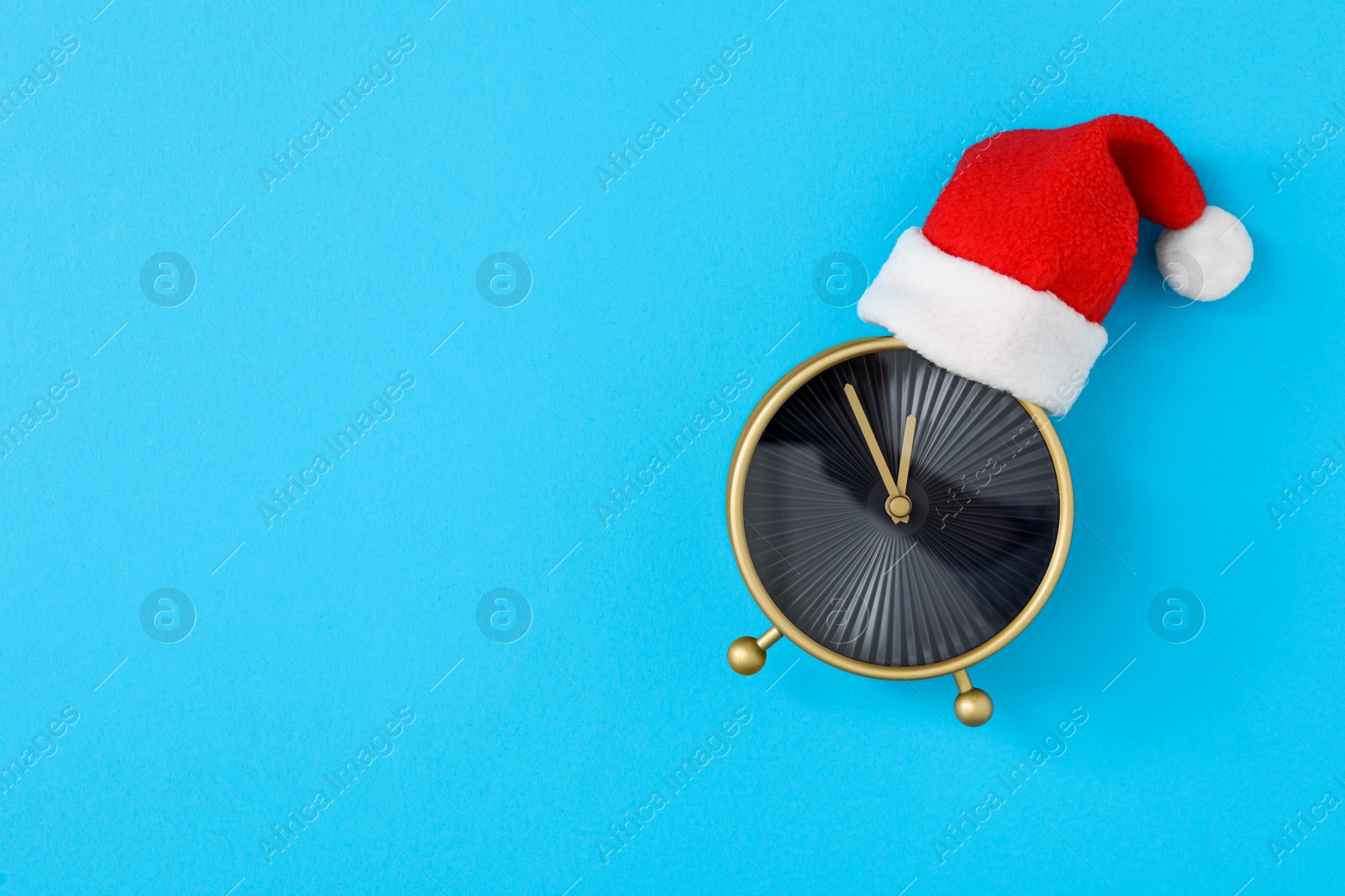 Photo of Alarm clock in Santa hat on light blue background, top view with space for text. New Year countdown