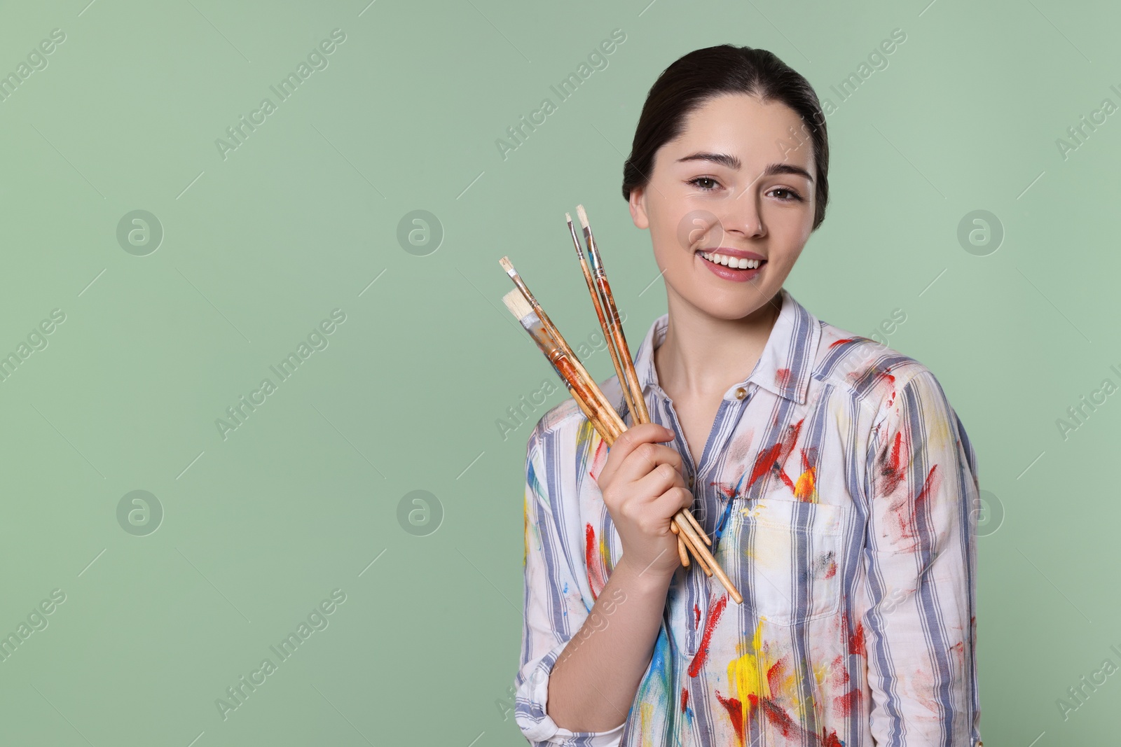 Photo of Woman with paintbrushes on pale green background, space for text. Young artist