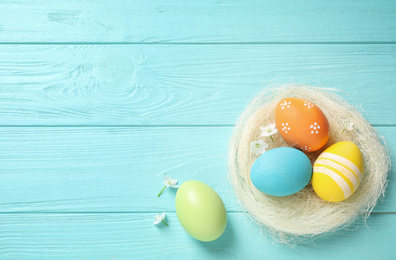 Photo of Colorful Easter eggs in decorative nest and flowers on light blue wooden background, flat lay. Space for text