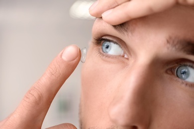 Photo of Young man putting contact lens in his eye on light background